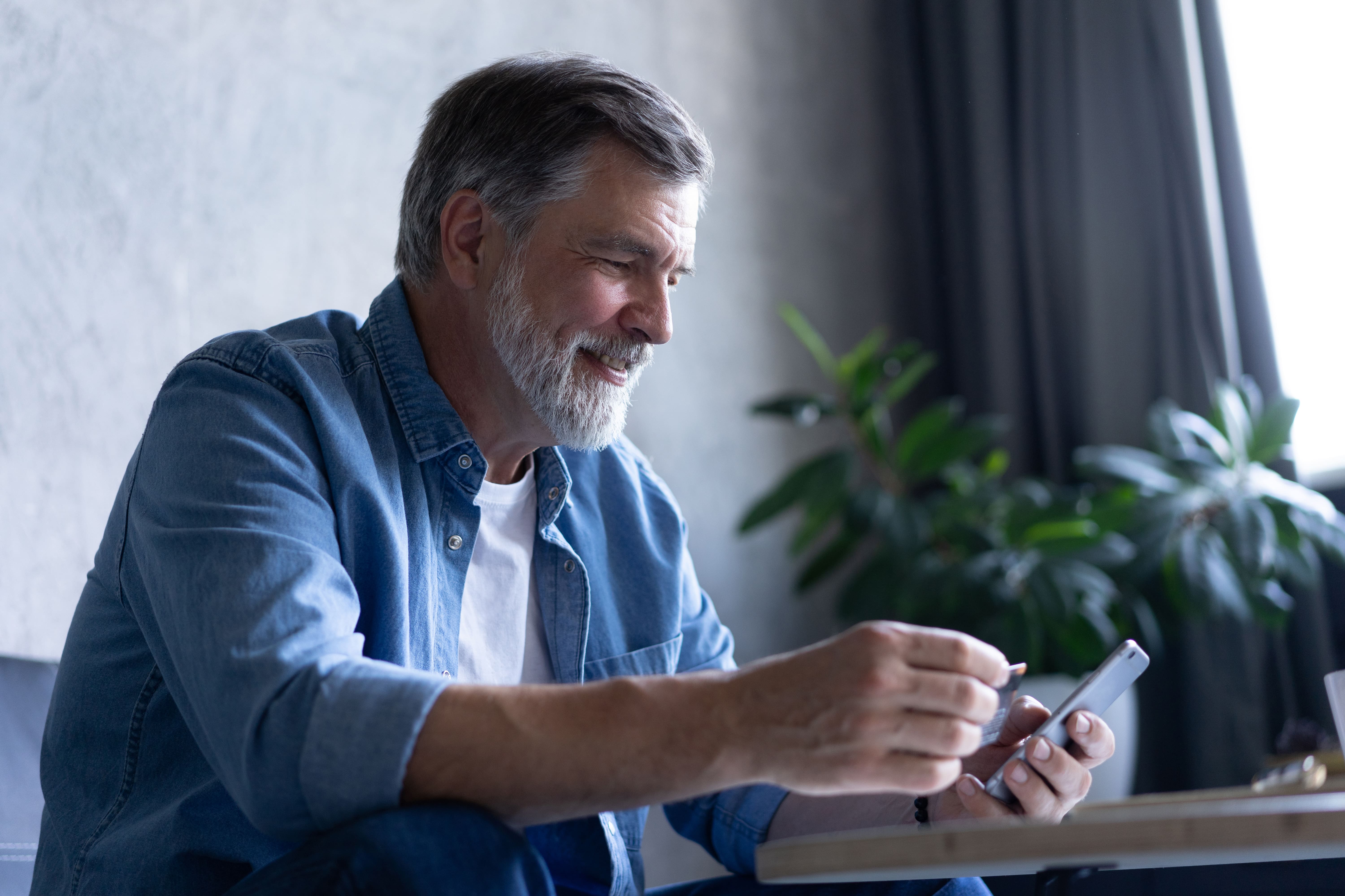 smiling-gray-haired-50s-man-pay-bills-online-using-modern-smartphone-gadget-credit-card-happy-mature-bank-client-make-internet-payment-purchase-cellphone-from-home-technology-concept-min